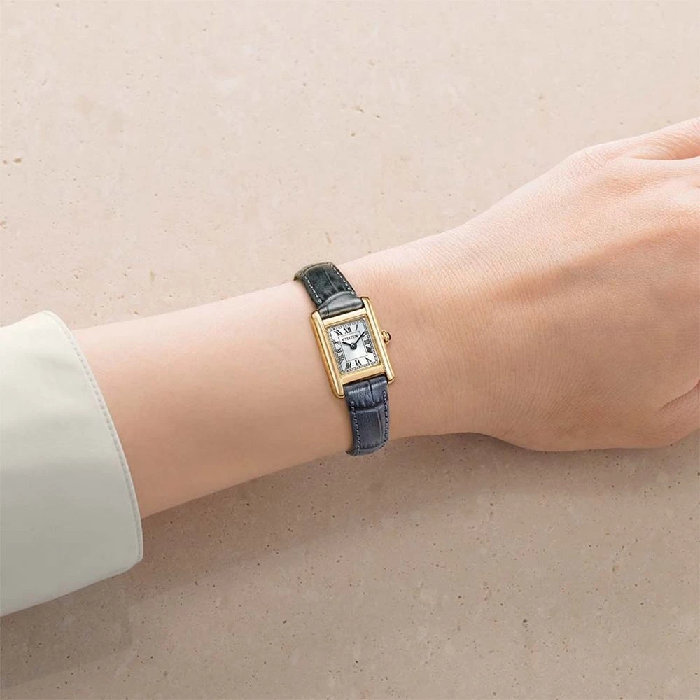 手腕上戴著 CITIZEN EG2799-18W：金色方形錶殼、白色羅馬數字錶盤與深藍色壓紋皮革錶帶
